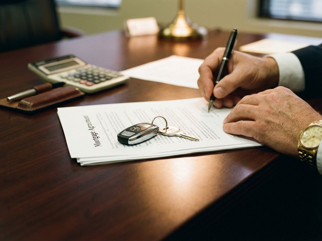Zakenman ondertekent hypotheekdocumenten met autosleutels op bureau, calculator en pen ernaast in kantoor